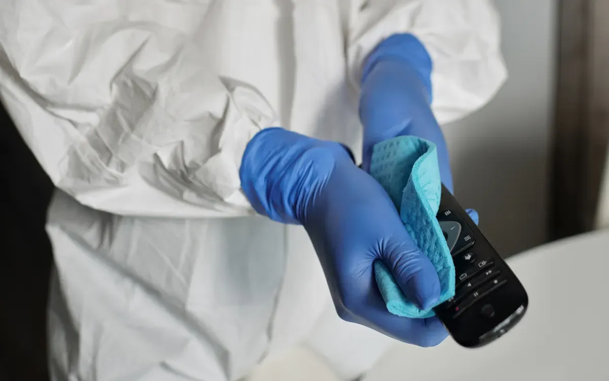 Professional cleaner wiping TV remote control with disinfecting cloth.
