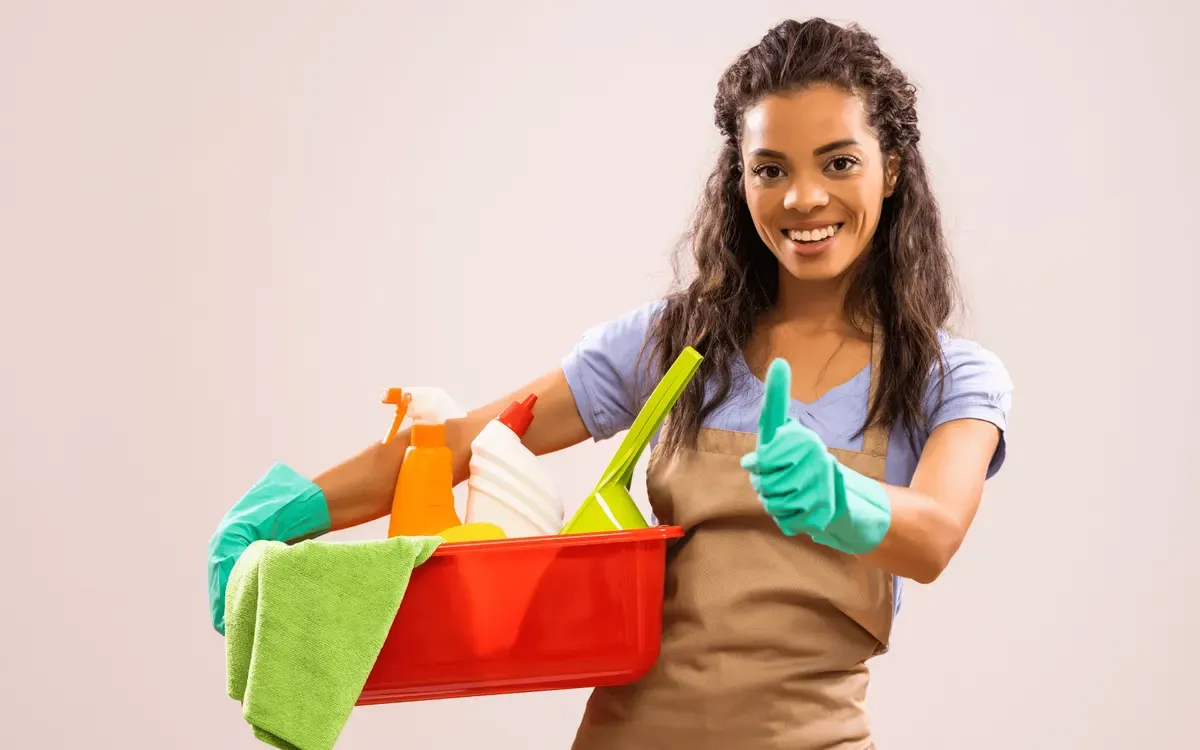 Residential cleaning service worker with cleaning products and gloves giving thumbs up for spotless home results.