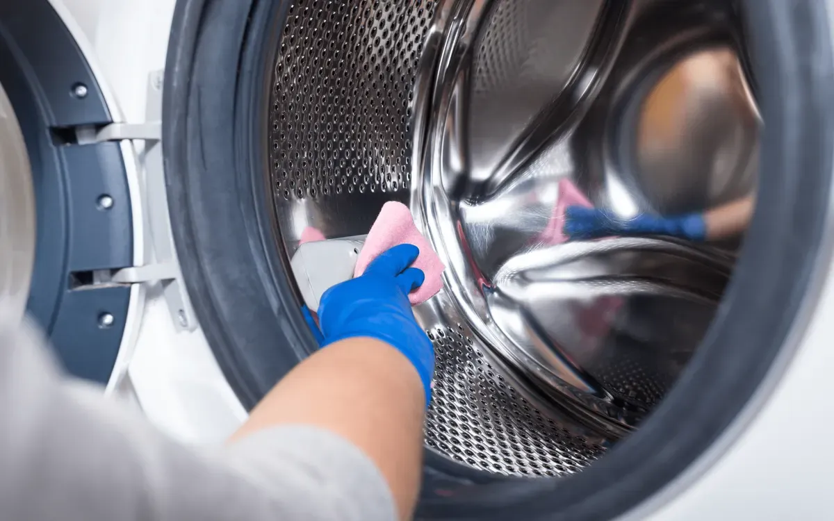 Next Day Cleaning professional wiping the inside of a washing machine drum with a pink cloth and blue gloves for deep appliance cleaning.