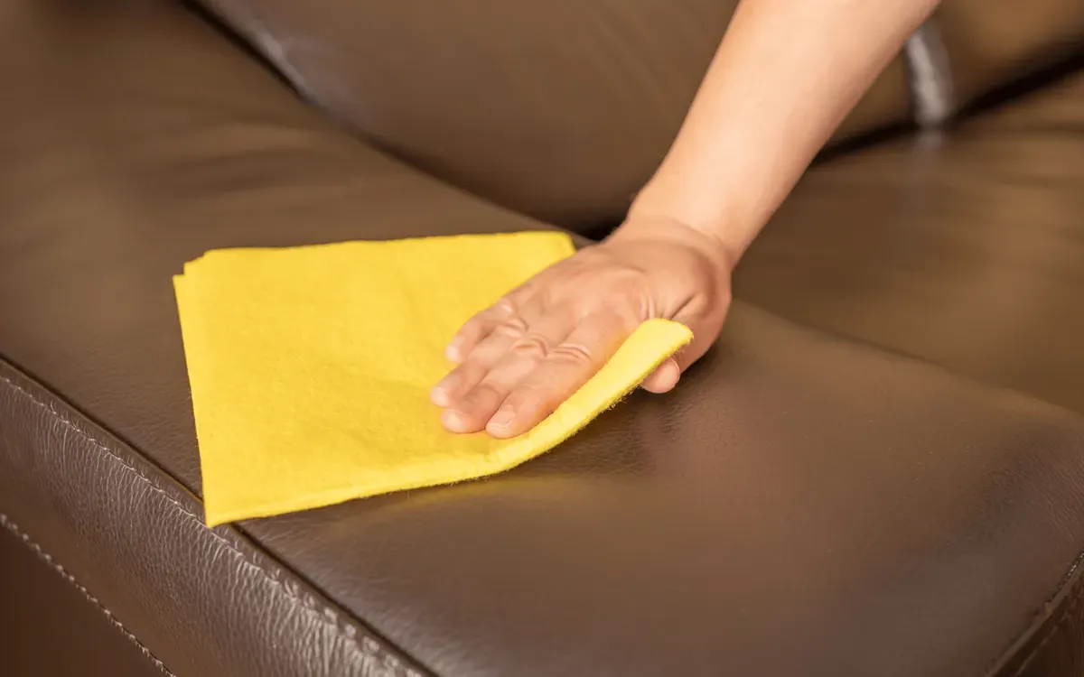 Cleaning service wiping and polishing leather sofa with microfiber cloth to remove dust and stains.